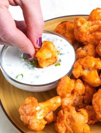 a hand dunking buffalo cauliflower into blue cheese sauce