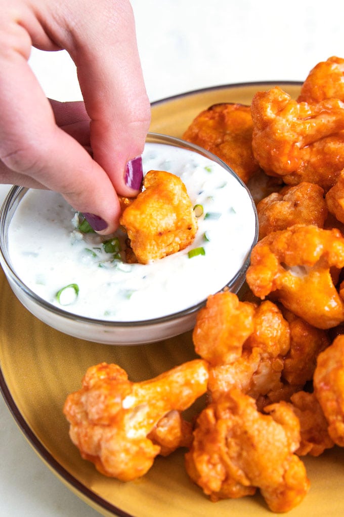 a hand dunking buffalo cauliflower into blue cheese sauce