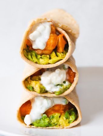 three wraps stacked on top of one another with sauce and avocado.