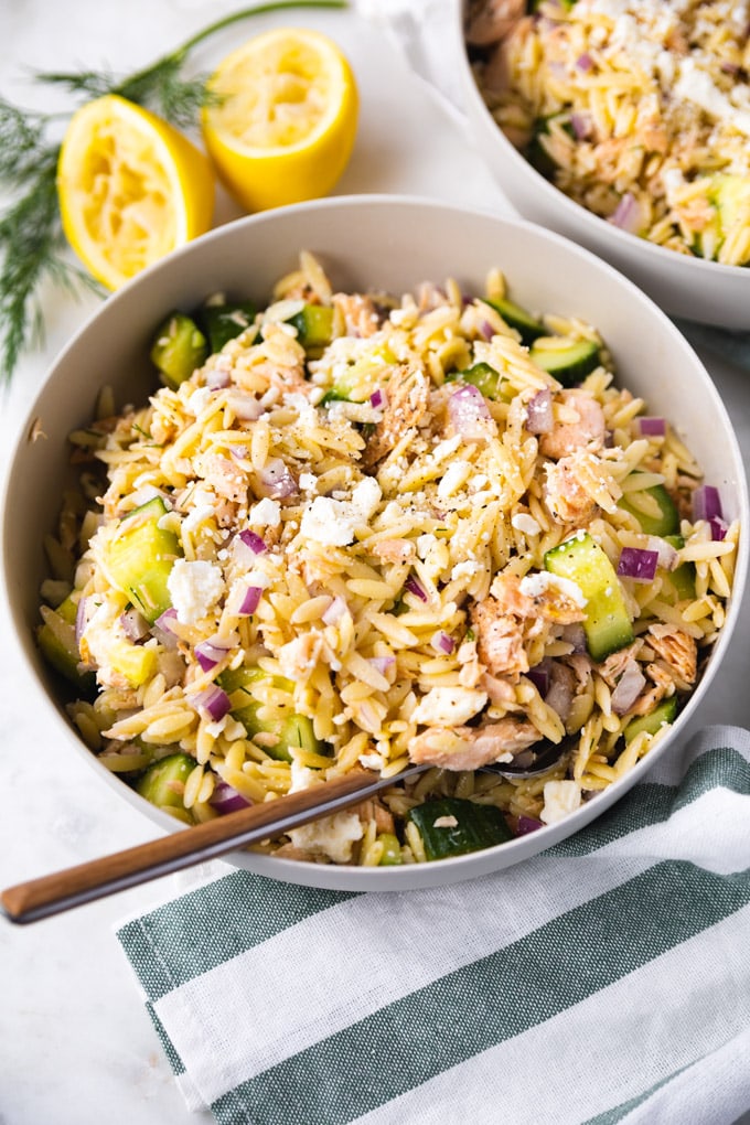 A bowl of salmon orzo salad  with lemons behind it.