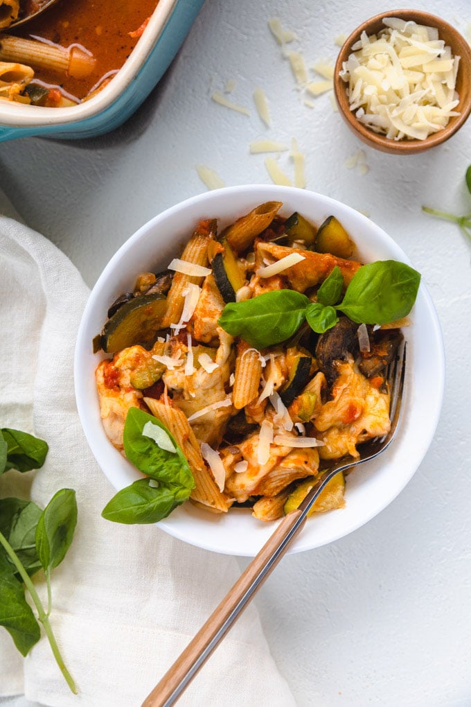 Chicken pasta bake in a bowl with cheese and basil on top.