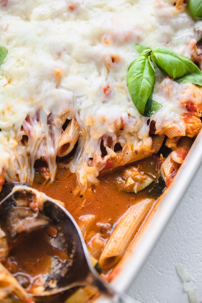 A spoon scooping out cheese and pasta from a casserole dish.