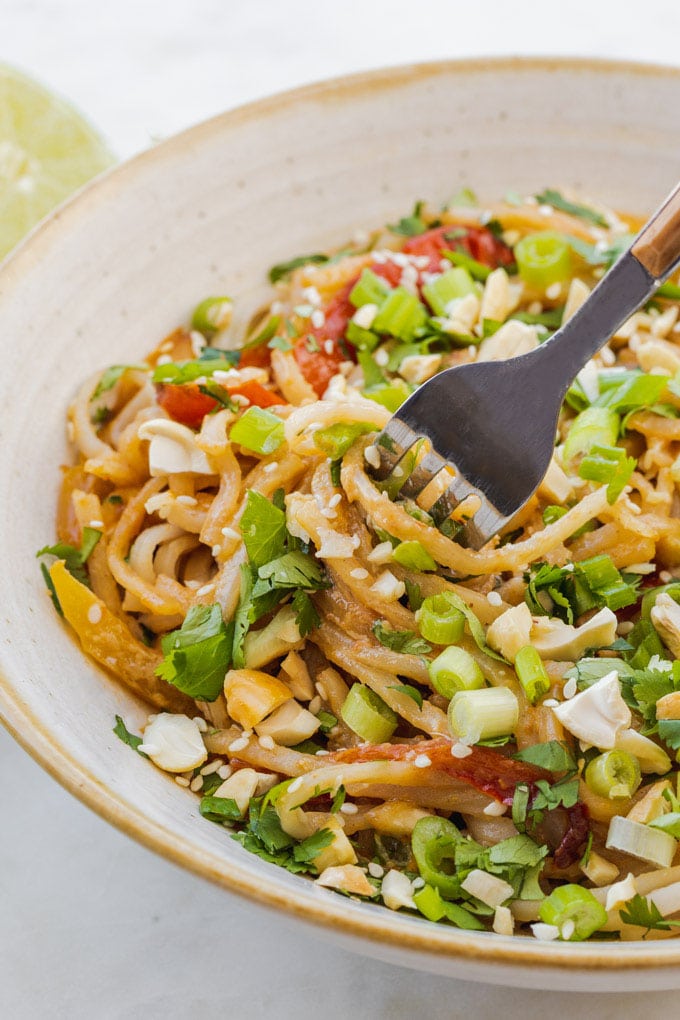 a bowl of noodles with pad thai sauce and fork in it. 