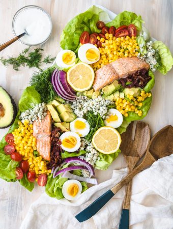 salmon Cobb salad on a plate with wooden serving spoons.