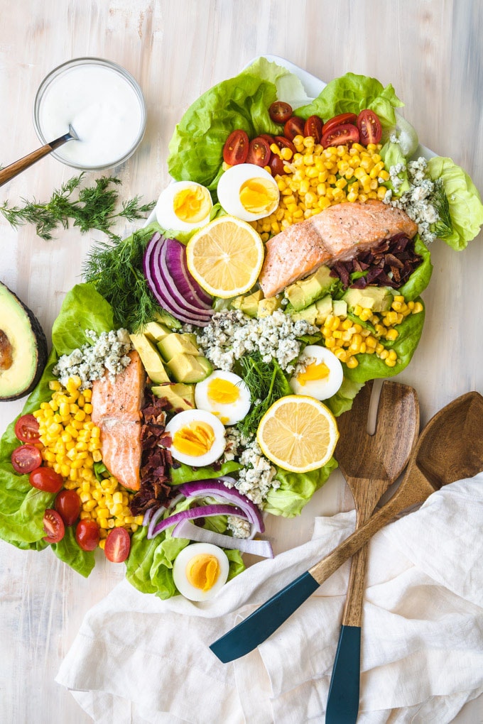 salmon Cobb salad on a plate with wooden serving spoons.