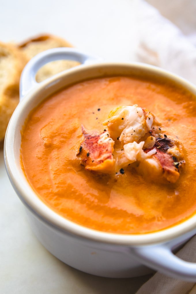 a bowl of creamy lobster bisque with bread on the side.