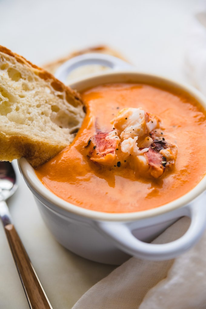 Bread being dunked into bisque in a bowl.