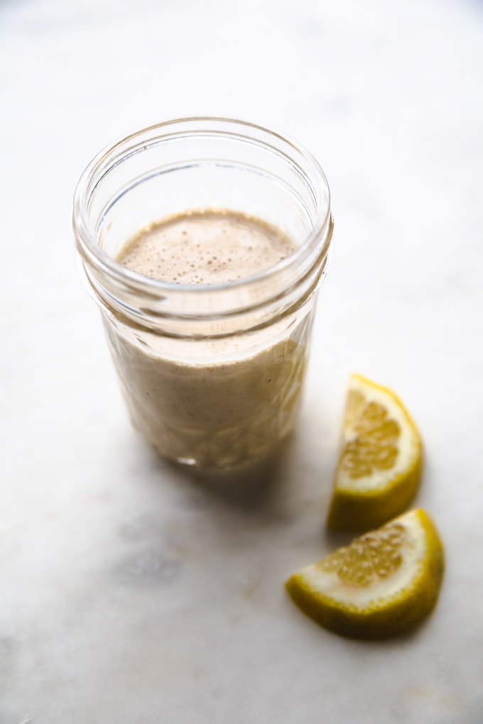 Lemon tahini dressing in a mason jar with lemons next to it. 