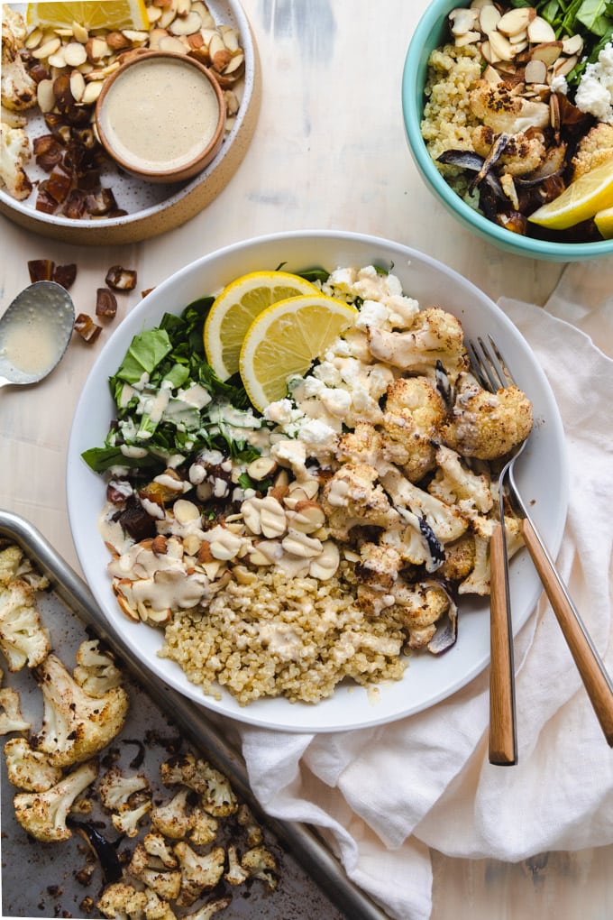 A bowl of healthy mediterranean cauliflower salad with toppings around it. 