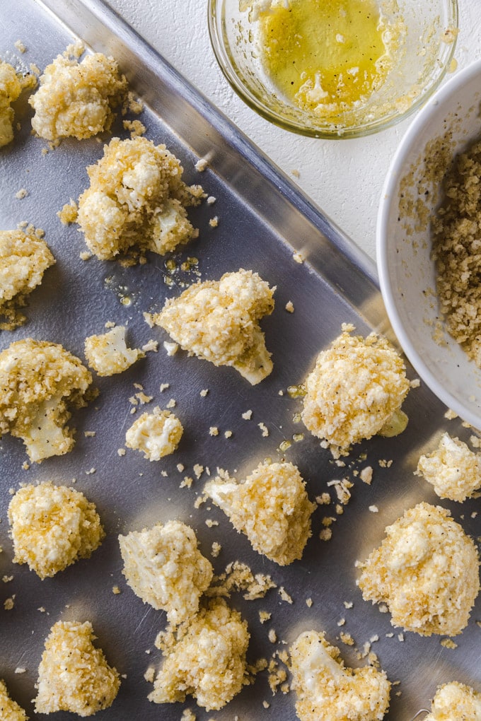 Uncooked cauliflower on a baking sheet with breadcrumbs and spices.