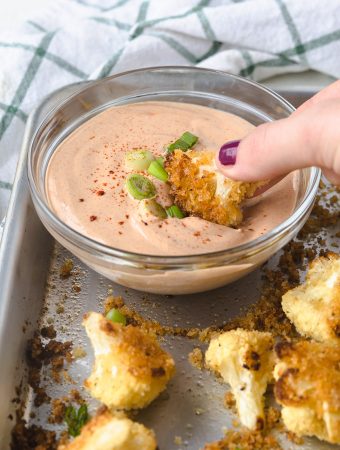 a hand dunking a cauliflower bite into yum yum sauce