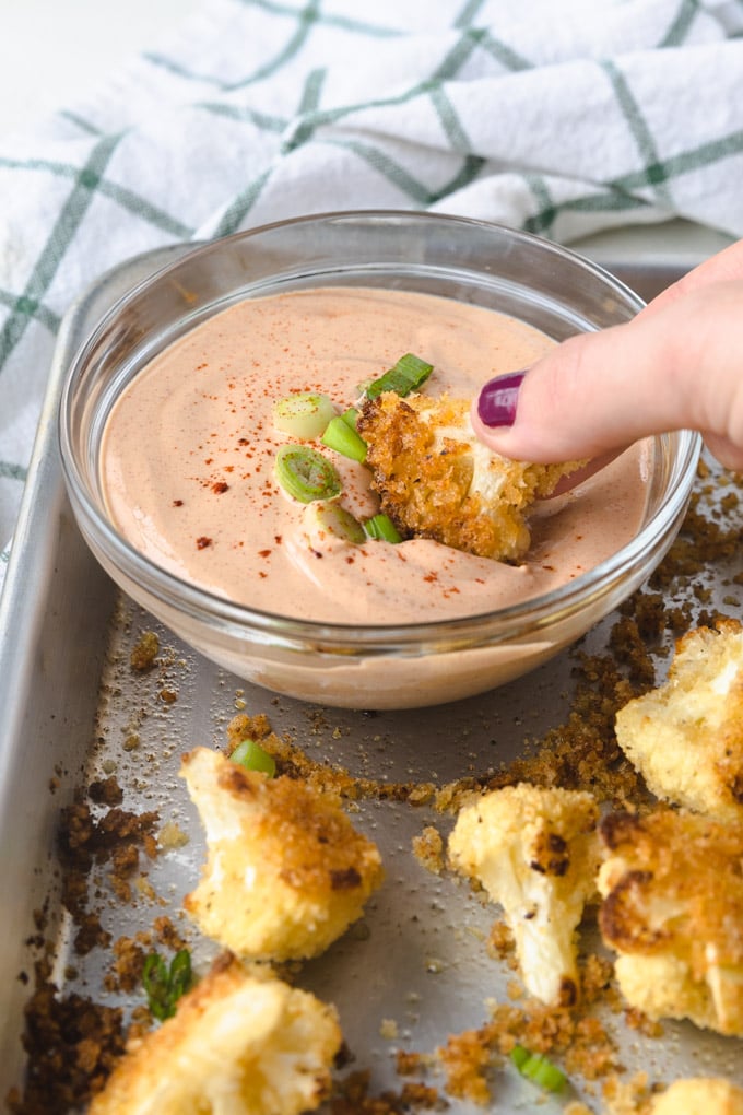 A cauliflower bite being dunked in yum yum sauce. 