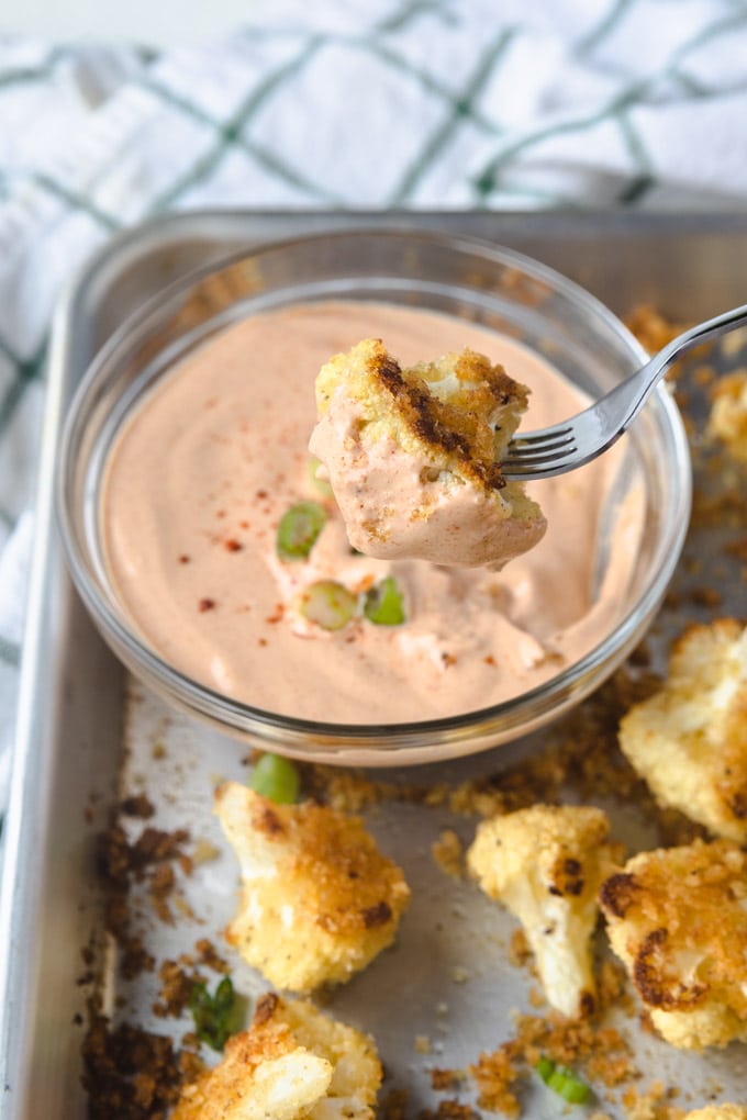 A fork holding crispy cauliflower with sauce.