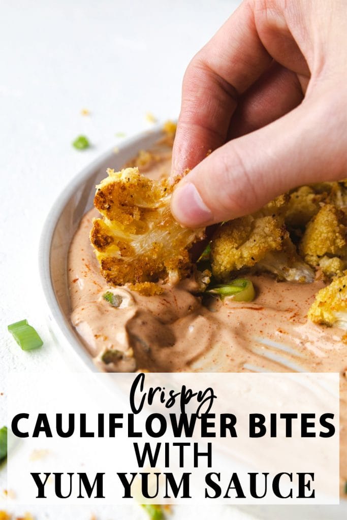 A hand with a cauliflower bite being dipped in sauce.