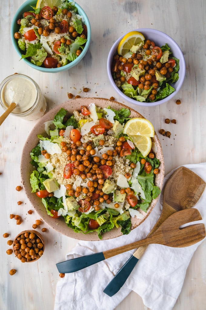 Bowl of salad with toppings over the bowl and spoons next to it. 