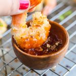 a hand dipping coconut shrimp in sauce.