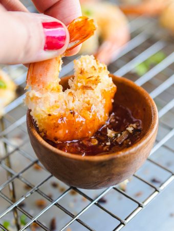 a hand dipping coconut shrimp in sauce.