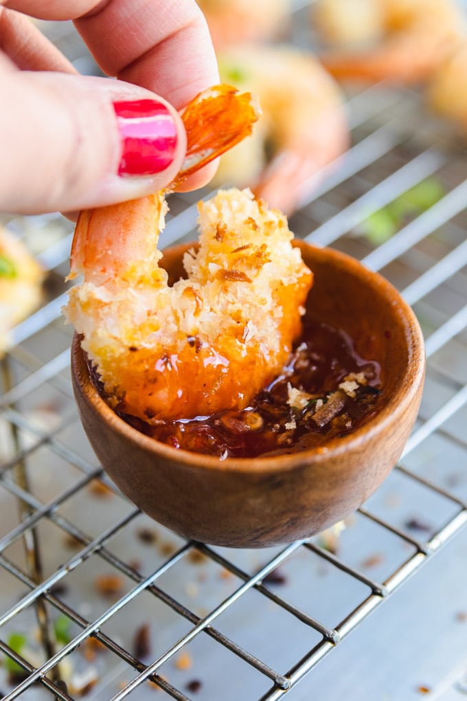 a hand dunking shrimp in sauce.