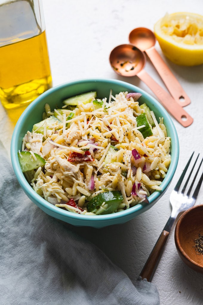 chicken pasta salad in a bowl with toppings around it. 