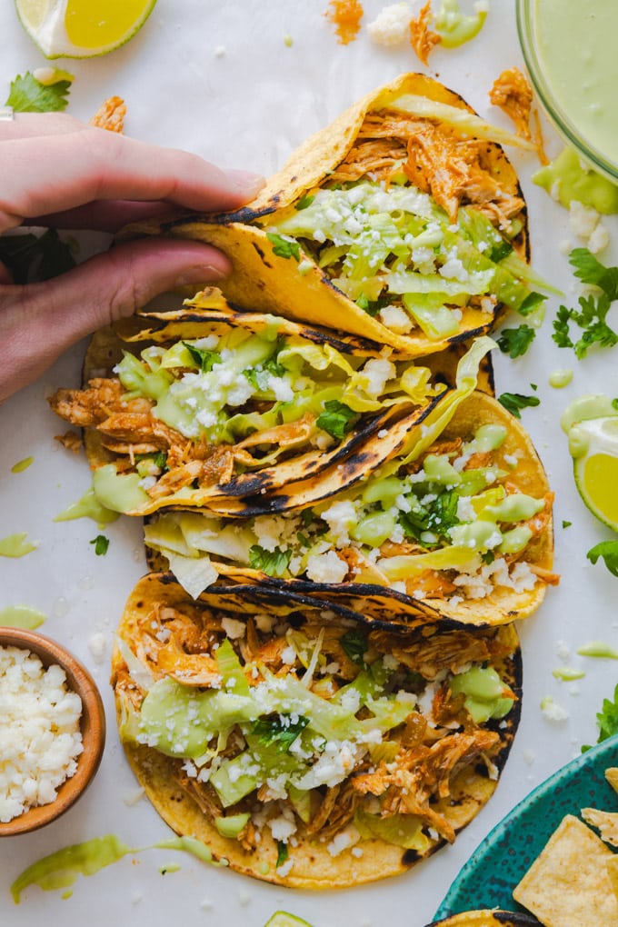 tacos with toppings around them and a hand grabbing one.