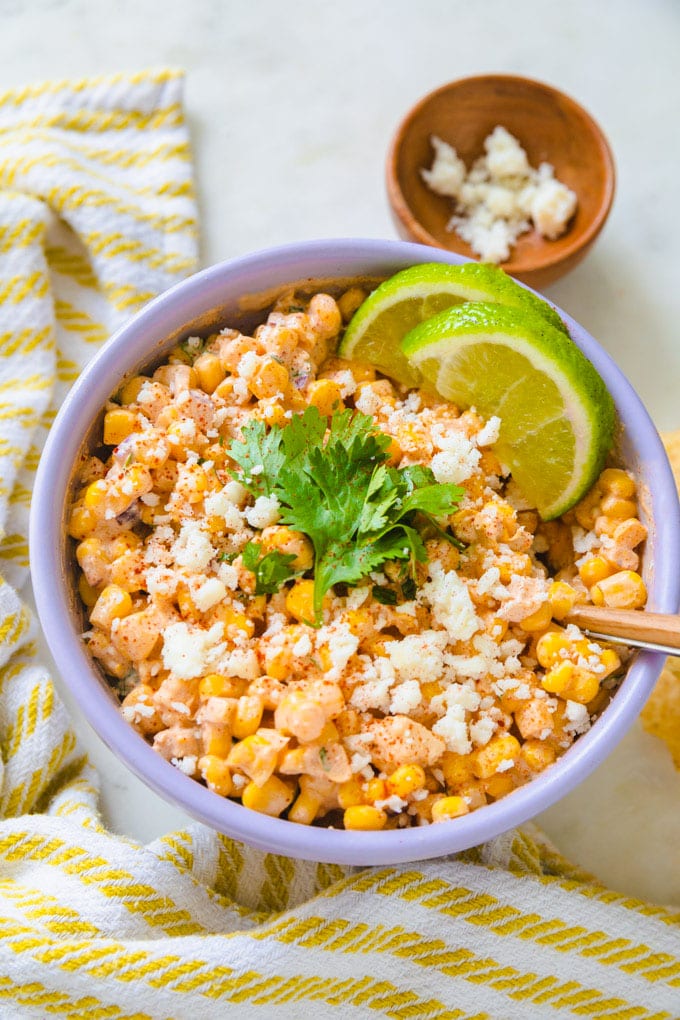 Mexican corn dip with limes and cheese in a bowl.