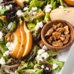 candied walnuts in a small bowl in a salad of goat cheese and lettuce.