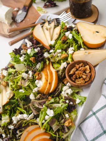 Pear and goat cheese Salad on a plate with toppings around it.