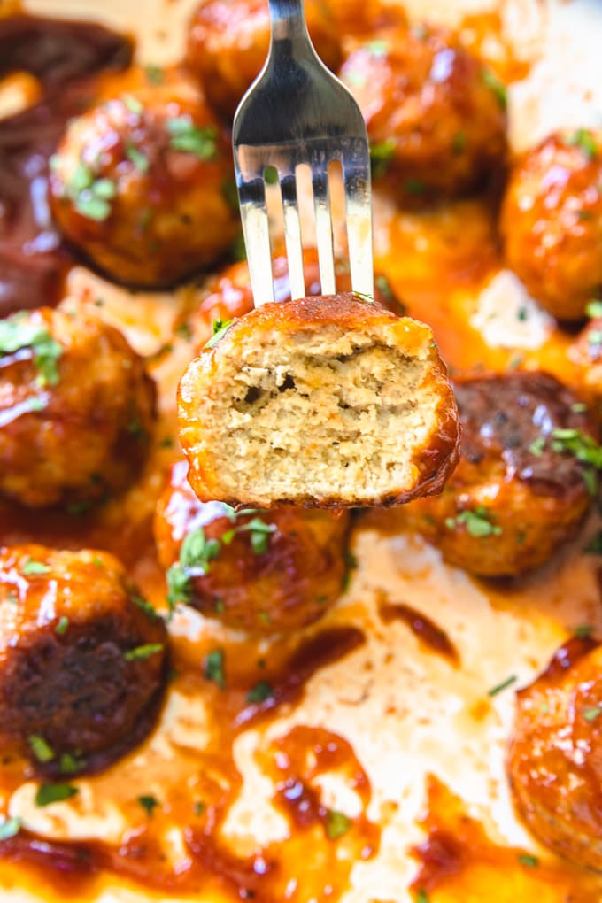 a chicken meatball with a fork stabbed in it and a bite mark. 