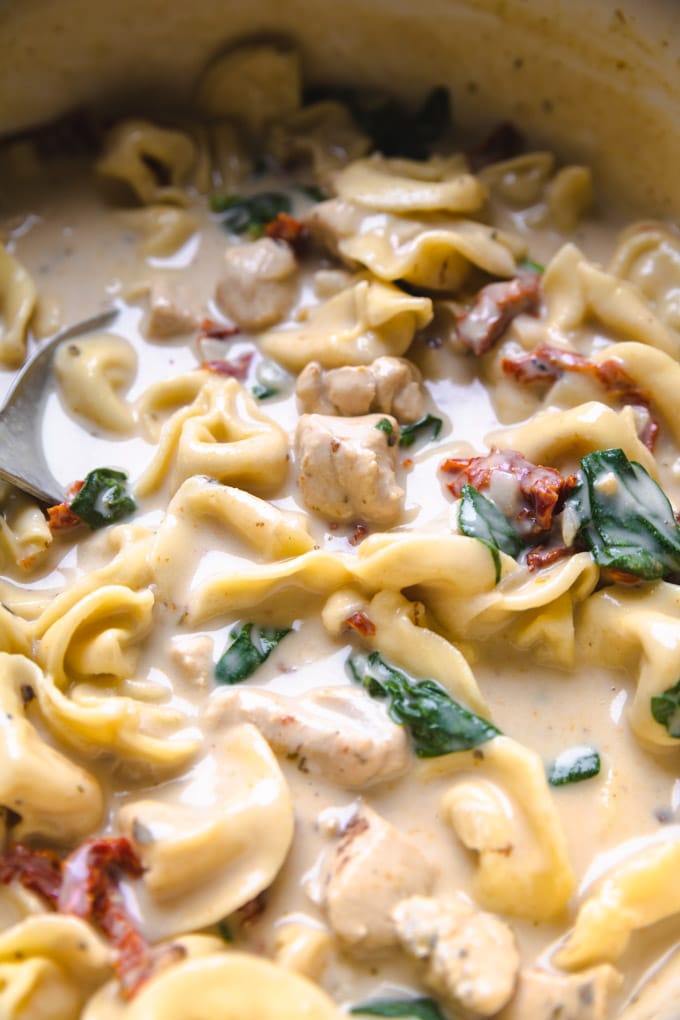 chicken tortellini soup in a pot with a large spoon.