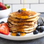 syrup being poured onto a stack of pancakes