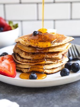 syrup being poured onto a stack of pancakes