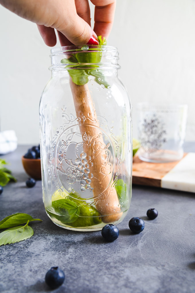 a hand putting basil leaves into a cocktail shaker. 