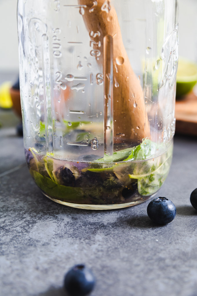 a mason jar with a wooden muddle in it and basil leaves. 