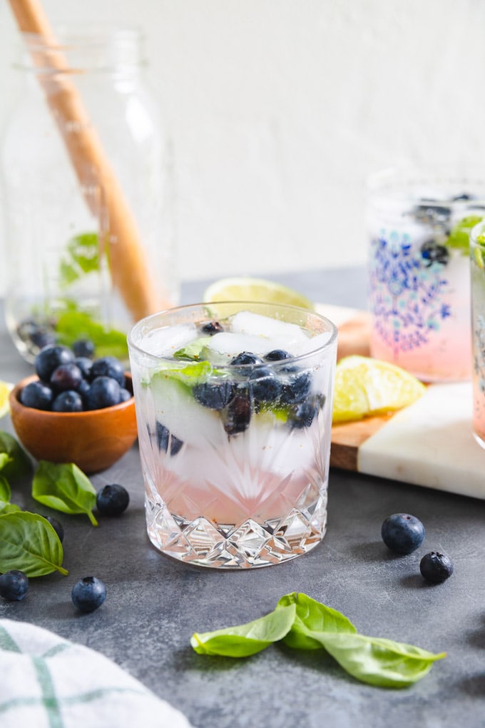 A glass full of basil and blueberries with lime.