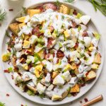 a plate of potato salad with a spoon and dressing next to it.