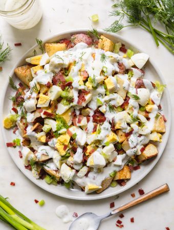 a plate of potato salad with a spoon and dressing next to it.