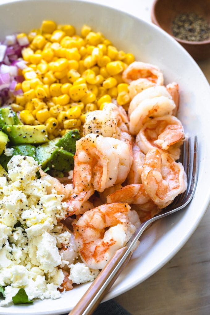 shrimp and feta in a bowl with a fork and other vegetables. 