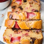 Sliced bread with strawberries and chocolate chips on a cutting board.