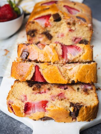 Sliced bread with strawberries and chocolate chips on a cutting board.