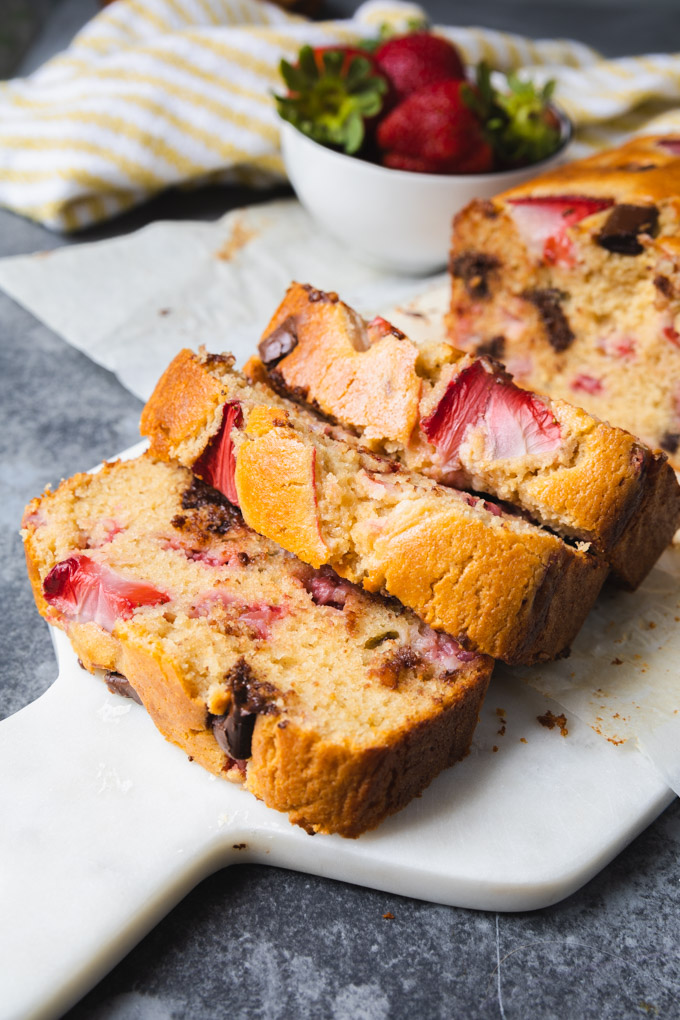 Strawberry chocolate bread on a marble board with strawberries in a cup and a towel. 