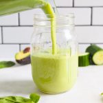 a mason jar being poured with a green smoothie.