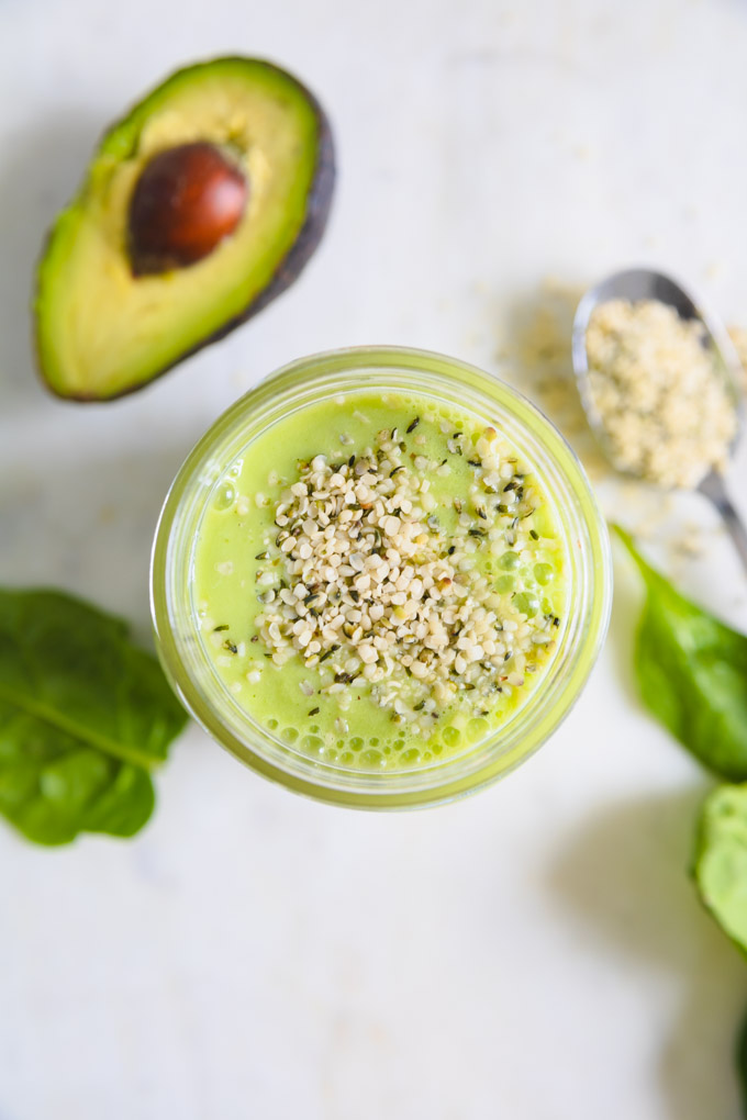 hemp seeds on top of a green smoothie with superfoods around it. 