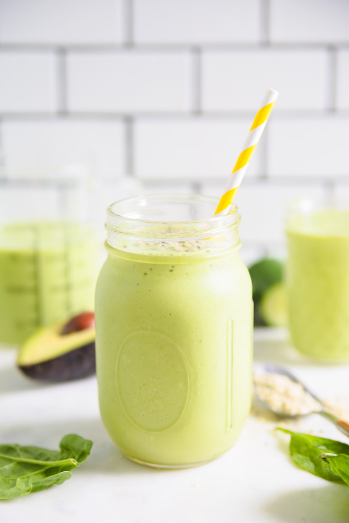 green smoothie in a mason jar with a straw and an avocado next to it.