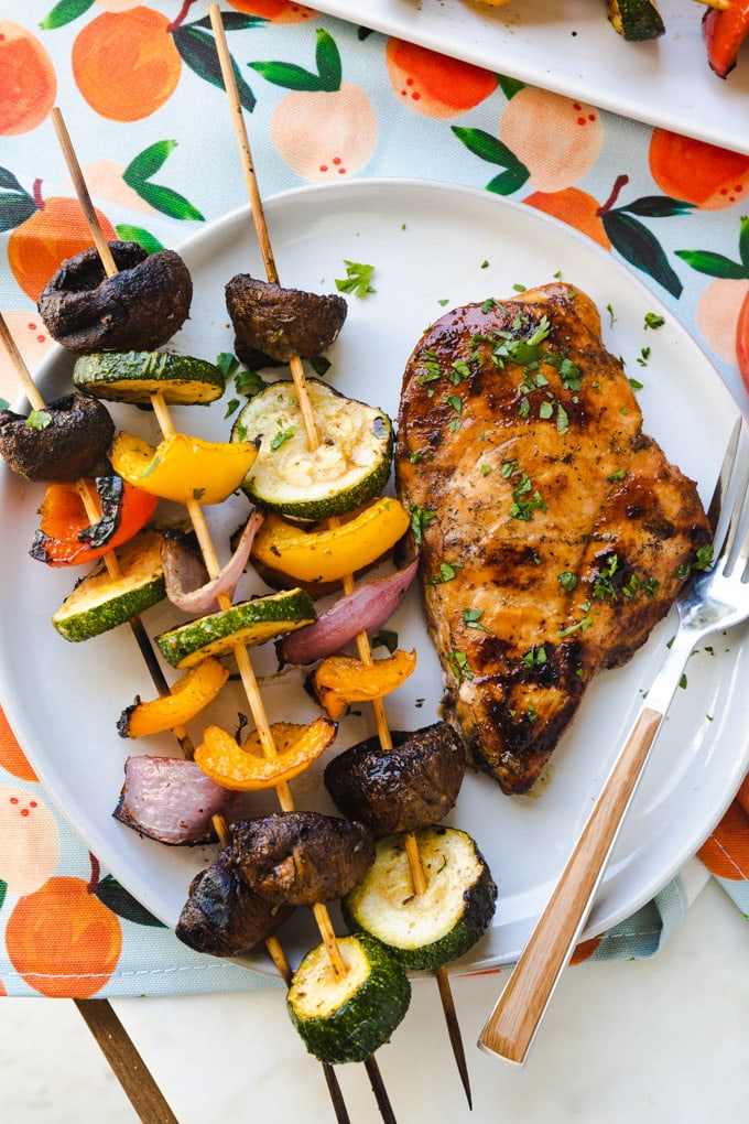 vegetable kabobs on a plate with a piece of grilled chicken. 