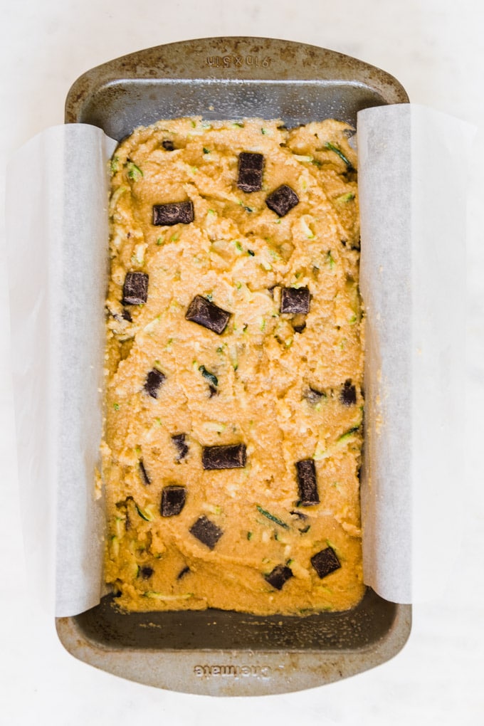 zucchini bread batter in a loaf pan with parchment paper. 