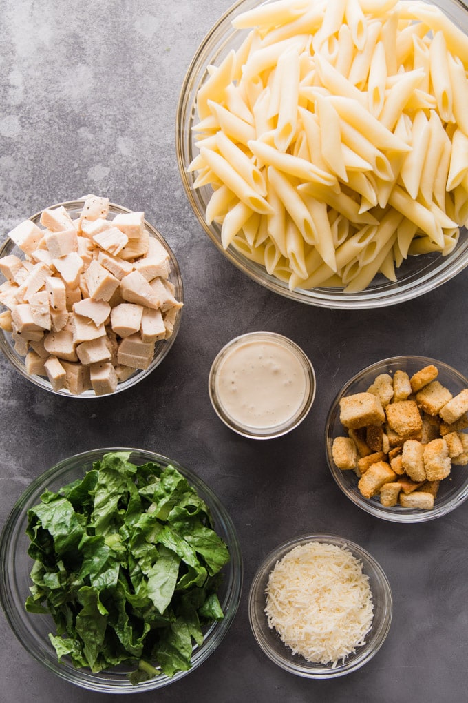 Ingredients for chicken caesar pasta salad in bowls.