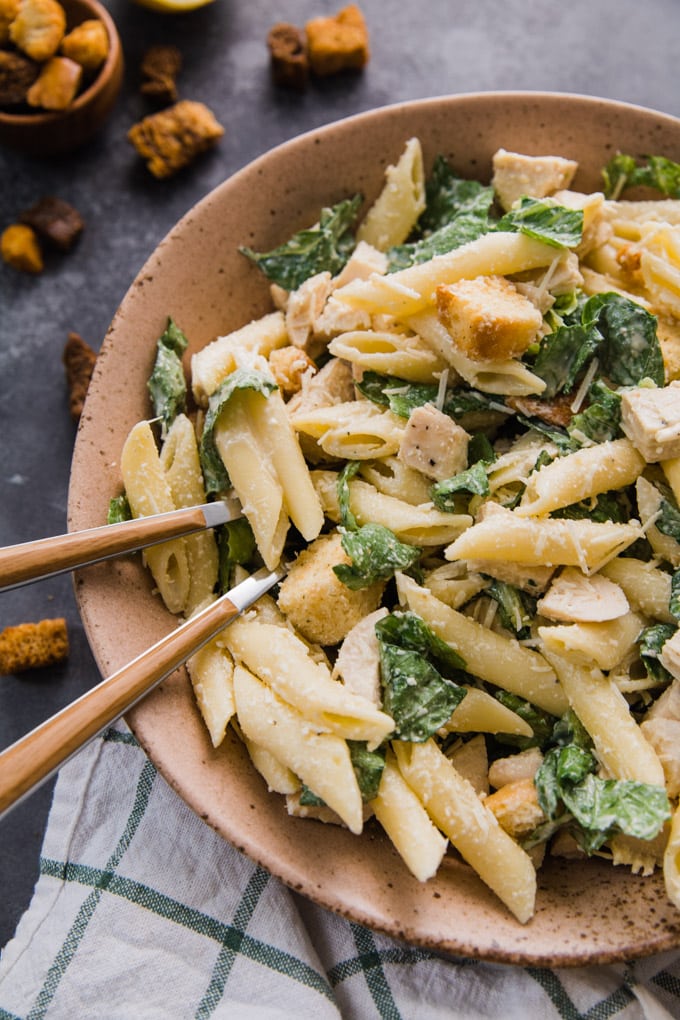 A bowl of chicken caesar pasta salad with two forks in it. 