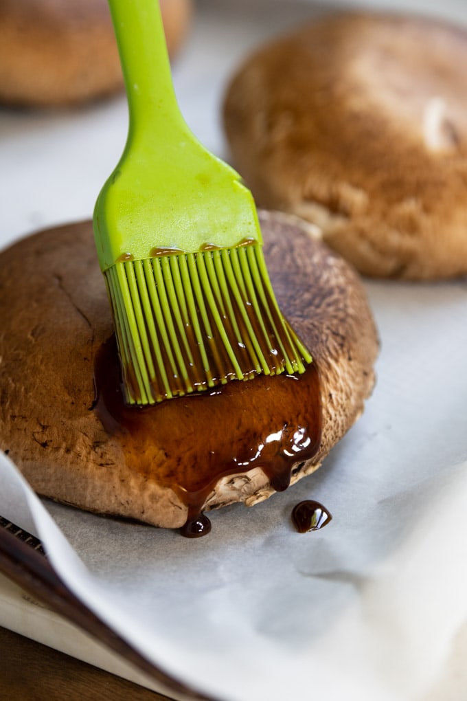 A brush with sauce brushing a portobello mushroom cap.