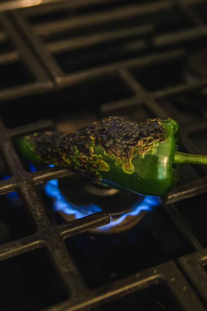 a poblano pepper being roasted oven an open flame.