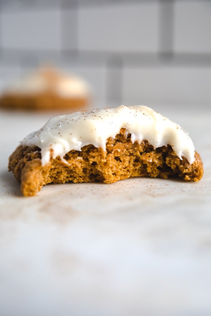 a bite taken out of a pumpkin cookie with frosting on top.